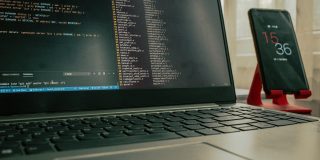 Funding restored for crucial cybersecurity program, but uncertainty remains | Code viewed on a MacBook Pro next to an iPhone