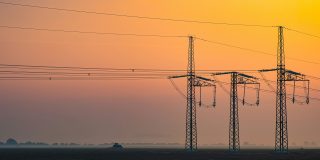 The MacBook Neo doesn't officially support fast charging, but beefier chargers help | Photo shows electricity pylons silhouetted against a sunrise