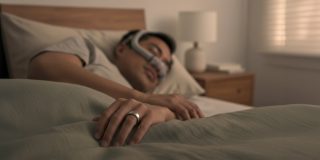 If your Oura smart ring detects sleep apnea, it can refer you to doctors | Photo shows someone wearing a CPAP mask in bed while wearing an Oura ring