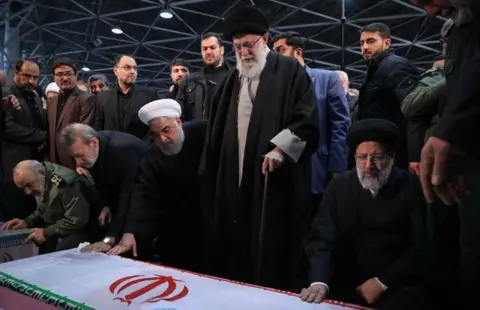 Anadolu via Getty Images Larijani and other politicians and clerics stand near an Iran flag. 