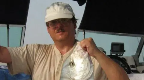 Lev Lakshtanov via MyMail.Ru A moustached man with spectacles and a white hat holding a fish by its head.