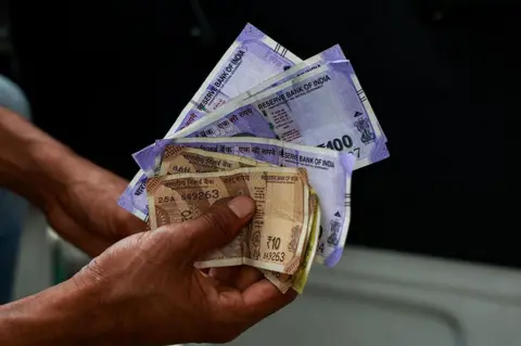 NurPhoto via Getty Images A driver holds 100 and 10 Rupee notes before refilling fuel at a petrol station in Baramulla, Jammu and Kashmir, India, on May 11, 2026. 
