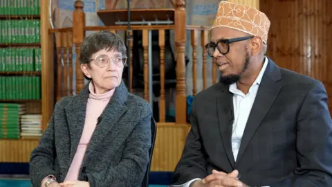 BBC / Brian Khisa Somali-American Imam Sharif Muhammad (R) and pastor Jane Buckley Farley (L) sitting with hands clasped for an interview in a mosque in Minneapolis