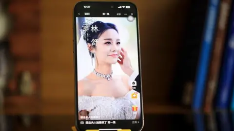 VCG via Getty Images A posed image of a mobile phone stood vertically, displaying a scene from a Chinese micro drama involving a bride smiling as the groom strokes her face