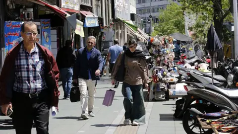 Getty Images People walking on a busy shopping street in Tehran, with a young woman carrying a shopping bag in the centre of the frame