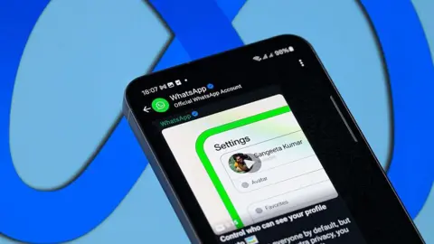 Getty Images WhatsApp displayed on a smartphone. A message from the Official WhatsApp Account on the app is displayed on the screen, with a video captioned "Control who can see your profile information". Meta's blue logo is in the background behind the phone.
