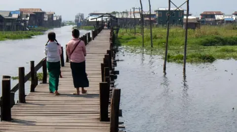 Getty Images Two girls viewed from behind walking on a footbridge in the village of Mang Thawk, Inle Lake