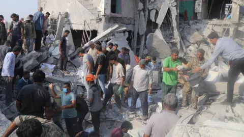 Reuters Crowds of men, some wearing helmets or masks, search the ruins of a building