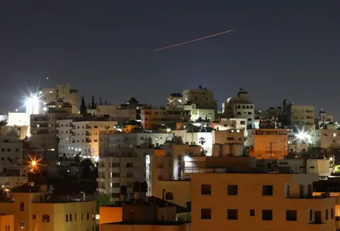 Anadolu via Getty Images Missiles launched from Iran toward Israel are seen in the sky over the West Bank city of Hebron on 7 June.
