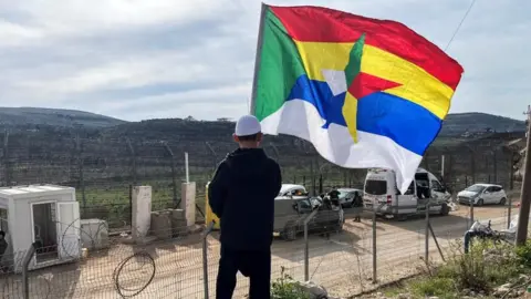 Reuters Boy holds a large Druze flag as he looks out towards the ceasefire line between the Israel-occupied Golan Heights and Syria (file photo)