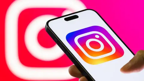 Getty Images Instagram's logo displayed on a smartphone, held in someone's hand, with a larger, blurred version of the logo in the background.