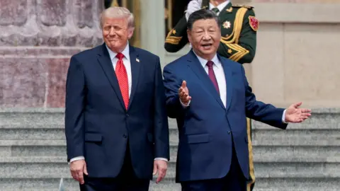 Reuters Xi stands with his hands outstretched as Trump smiles on the stairs. A soldier can be seen standing behind them