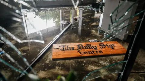 NurPhoto via Getty Images Attackers vandalised and torched The Daily Star office, causing extensive damage. A shattered sign lies amid broken glass at reception.