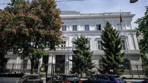 Getty Images Wide shot of the Russian embassy in Vienna showing three cars parked in front and a Russian flag on a flag pole outside the building.