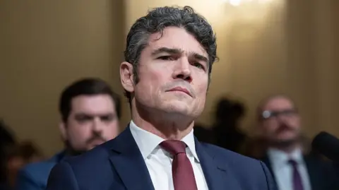 AFP via Getty Images Kent during a committee hearing, wearing a dark blue suit and a red tie, with a serious expression