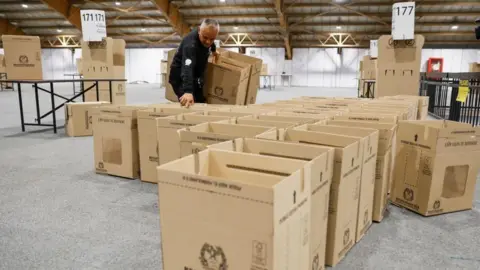 EPA An election worker with a dark jacket arranges cardboard ballot boxes in a large hall