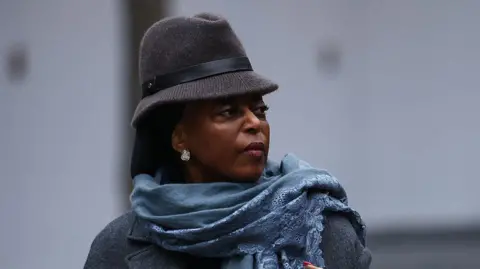 Getty Images Headshot of Diezani Alison-Madueke looking off-camera wearing a grey brimmed hat with a blue scarf and grey coat.