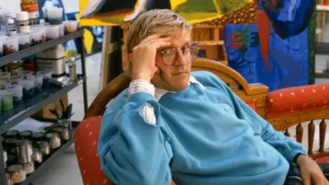 Getty Images David Hockney in his Studio in California in 1987 wearing a blue jumper relaxing on a chair with his hand to his face 
