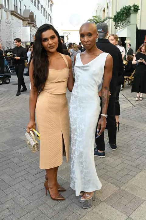 Getty Images Mindy Kaling standing on the left in a beige dress and Cynthia Erivo standing next to her in a white dress at the Vogue World show