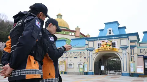 YONHAP/EPA/Shutterstock Two policemen looking at a remote control, standing in front of the entrance to O-World theme park