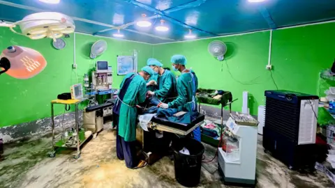 BBC/Darren Conway The operating theatre, with three doctors wearing green scrubs and facemasks