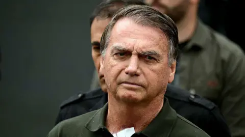 Getty Images Police escort Jair Bolsonaro, who wears a green polo top, from hospital
