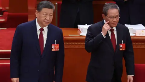 Getty Images China's President Xi Jinping standing next to Premier Li Qiang as they take their seats at the opening session of the National People's Congress (NPC) at the Great Hall of the People in Beijing on 5 March