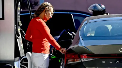 Shutterstock A woman pumps gas at an Exxon station in Washington, D.C. on April 7, 2026. 