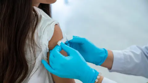 Getty A young girl is has a plaster put on her arm by a person wearing blue gloves