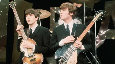 UPI/Bettmann via Getty Images British Rock musicians Paul McCartney (left) and John Lennon perform on the set of 'The Ed Sullivan Show' in 1964. The photo was taken during rehearsals for the group's debut performance on the show the following day
