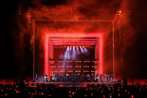 BIGHIT MUSIC AND NETFLIX A wide shot of the stage turned red with dancers on stage and fans in the crowd