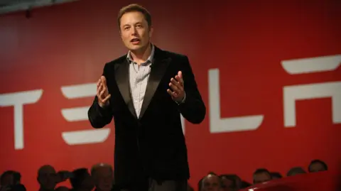 Alamy Elon Musk in suit talks to crowd at Tesla event