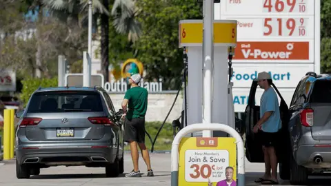 Getty Images Two drivers wearing shorts and t shirts fill up their cars with petrol. 