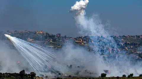 Reuters Two explosions of white smoke in front of a hillside - the Lebanese side of the border with Israel