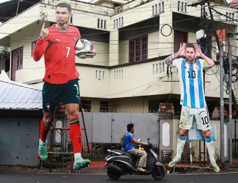 NurPhoto via Getty Images A man rides a scooter past giant cutouts of Portugal's Cristiano Ronaldo and Argentina's Lionel Messi displayed along a roadside in Kochi, India, on June 9, 2026, ahead of the 2026 FIFA World Cup. (Photo by Sivaram Venkitasubramanian/NurPhoto via Getty Images)