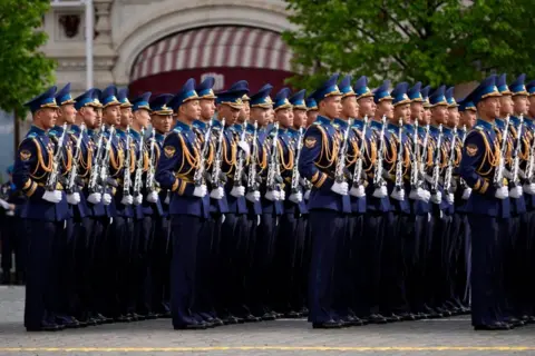 EPA/Shutterstock North Korean soldiers stand in rows wearing dark blue uniforms with gold decorations and holding guns.