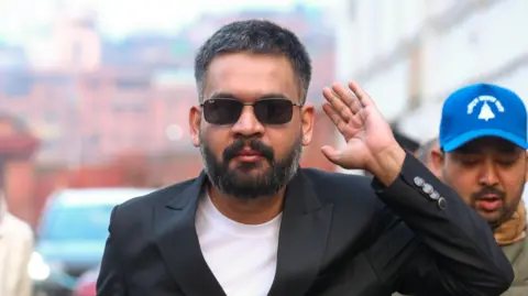 Getty Images Balen Shah, in a black coat and sunglasses, waves at supporters