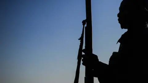 Getty Images A silhouette of a man holding a rifle at nighttime. His face, clothes and identity are not distinguishable.