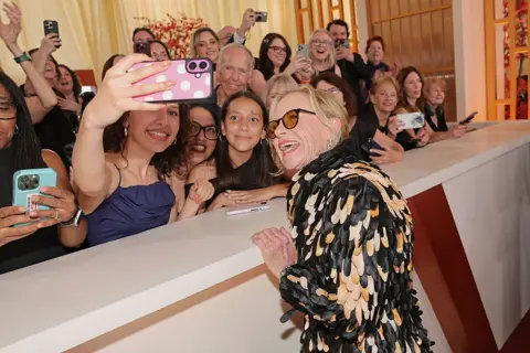 Getty Images Amy Madigan poses for a selfie with people behind a partition on the 98th Oscars red carpet at the Dolby Theatre 