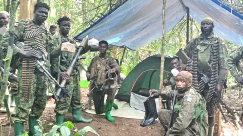 UPDF A group of Ugandan soldiers in camouflage holding weapons and magazines of bullets stand in a group looking at the camera.