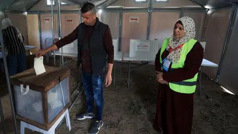 Getty Images A man places a ballot into a box in a makeshift polling station in Gaza while a female election officials looks on