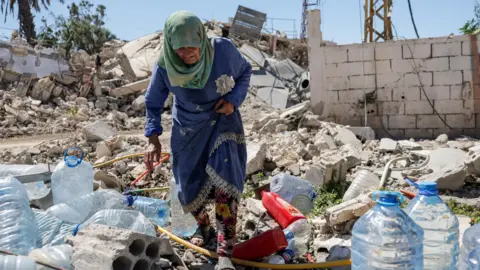 Reuters Khadija Amara fills a jerrycan with water as she sits among the rubble of a house, which was damaged by an Israeli strike, in Qlaileh in the Tyre district, southern Lebanon
