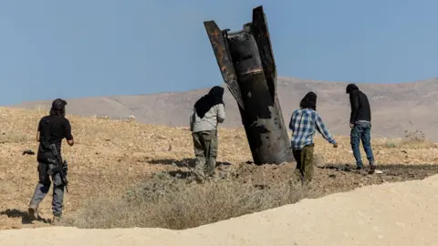 Reuters Israeli settlers stand next to part of an Iranian ballistic missile protruding from the ground in the Israeli-occupied West Bank (8 June 2026)