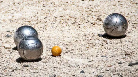 Getty Images Three metal Pétanque boules sit apart from eachother on a gravel floor, all three are shining in the sunlight.