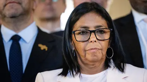 Getty Images Delcy Rodriguez wearing a white suit and black framed glasses. 