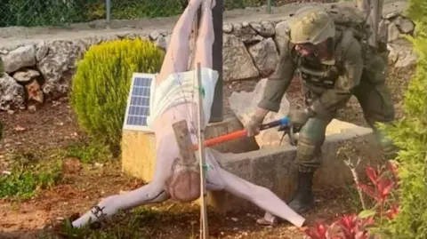 Reuters An Israeli soldier uses an implement to hit the face of an upturned statue of Jesus Christ in south Lebanon (April 2026)