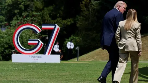 Reuters Donald Trump and Giorgia Meloni, both wearing suits, walk away from the camera with the G7 logo to their left.