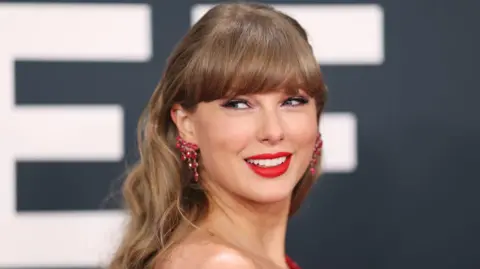 Getty Images A photograph of Taylor Swift looking over her shoulder and smiling, wearing red earrings.