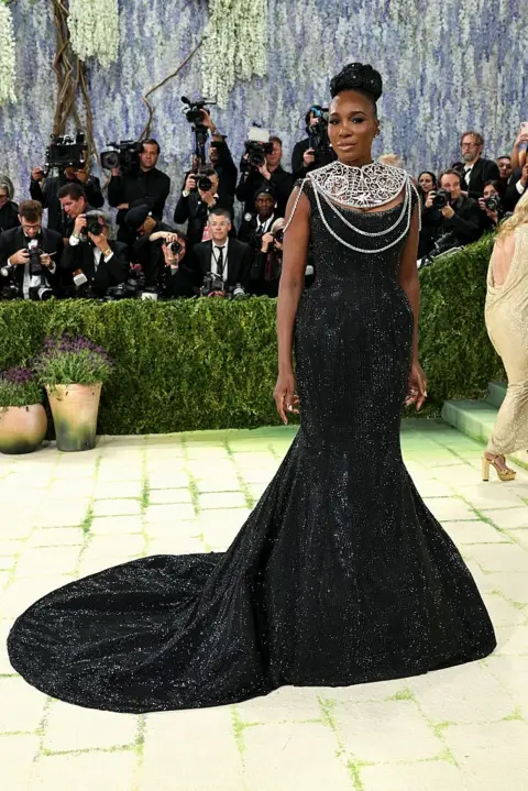 Getty Images Venus Williams wears a black, sparkling gown with a flared train, but the star of the outfit is her large silver neck adornment.