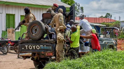 Reuters Medical staff climb aboard a military vehicle on the grounds of Rwampara General Hospital. One soldier pictured in camouflage has a large machine gun.